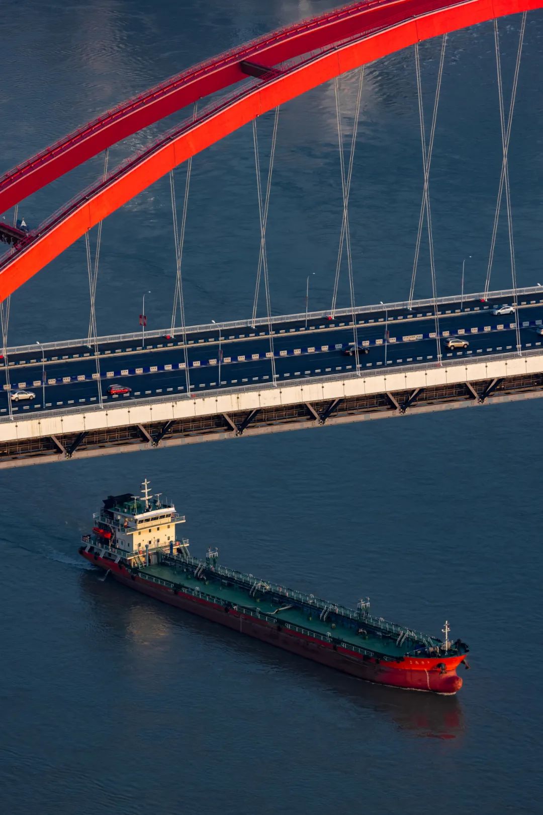 阳光打亮着菜园坝长江大桥的弧形桥拱，与驶来的红色货轮，恰好形成一致的色彩呼应。